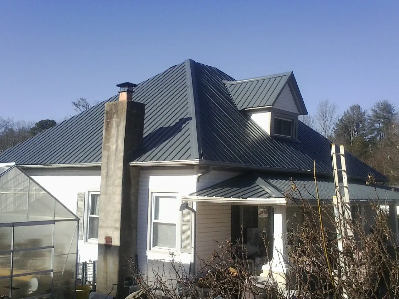 Dark blue standing seam metal roof on a white farmhouse with dormer — Slate & Tile Roof Repair by Roofing Brothers in Purchase