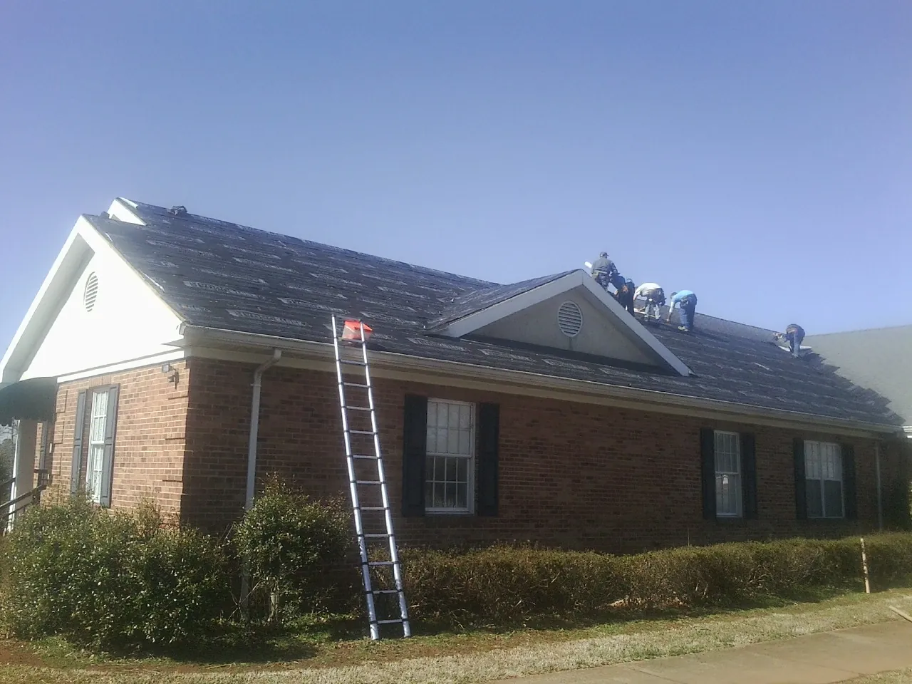 Crew tearing shingles off a brick ranch roof with a ladder set — Emergency Roof Repair work by our crew in Purchase