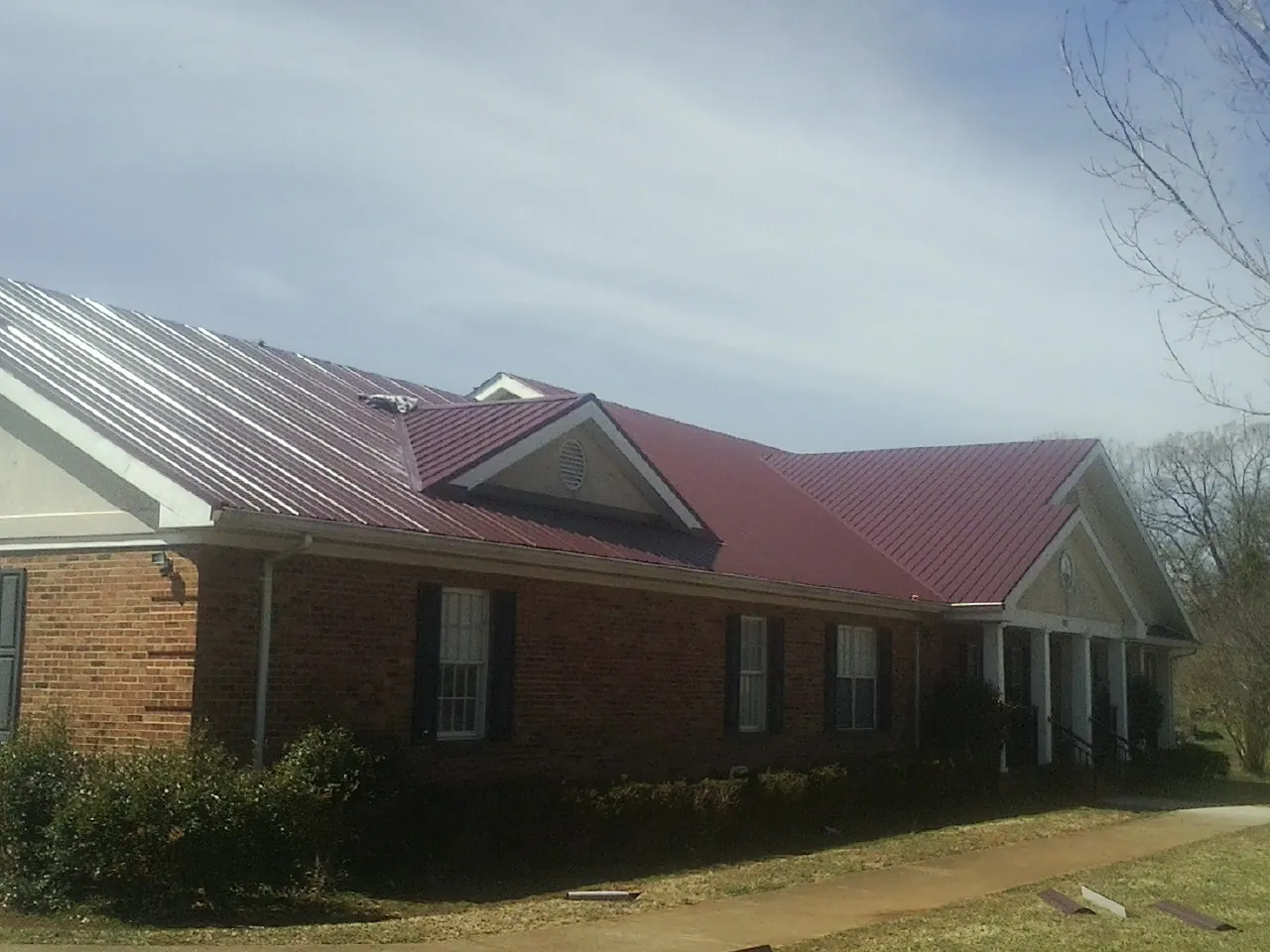 Red metal roof with gabled entries on a long brick building, from a Hail Damage Roof Repair job in Purchase