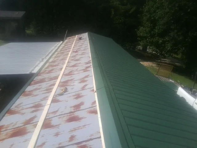 Old rusted panels beside newly installed green metal roofing — Wind Damage Roof Repair by Roofing Brothers in Purchase