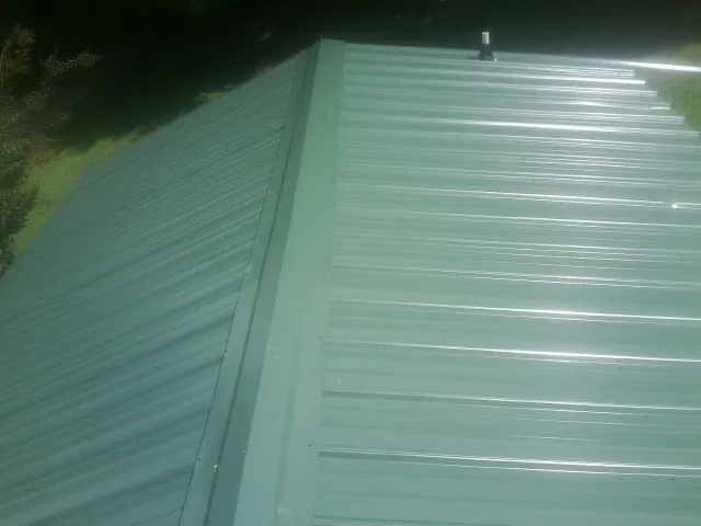 New green metal panels meeting at the ridge of a roof — Flat Roof Repair work by our crew in Purchase