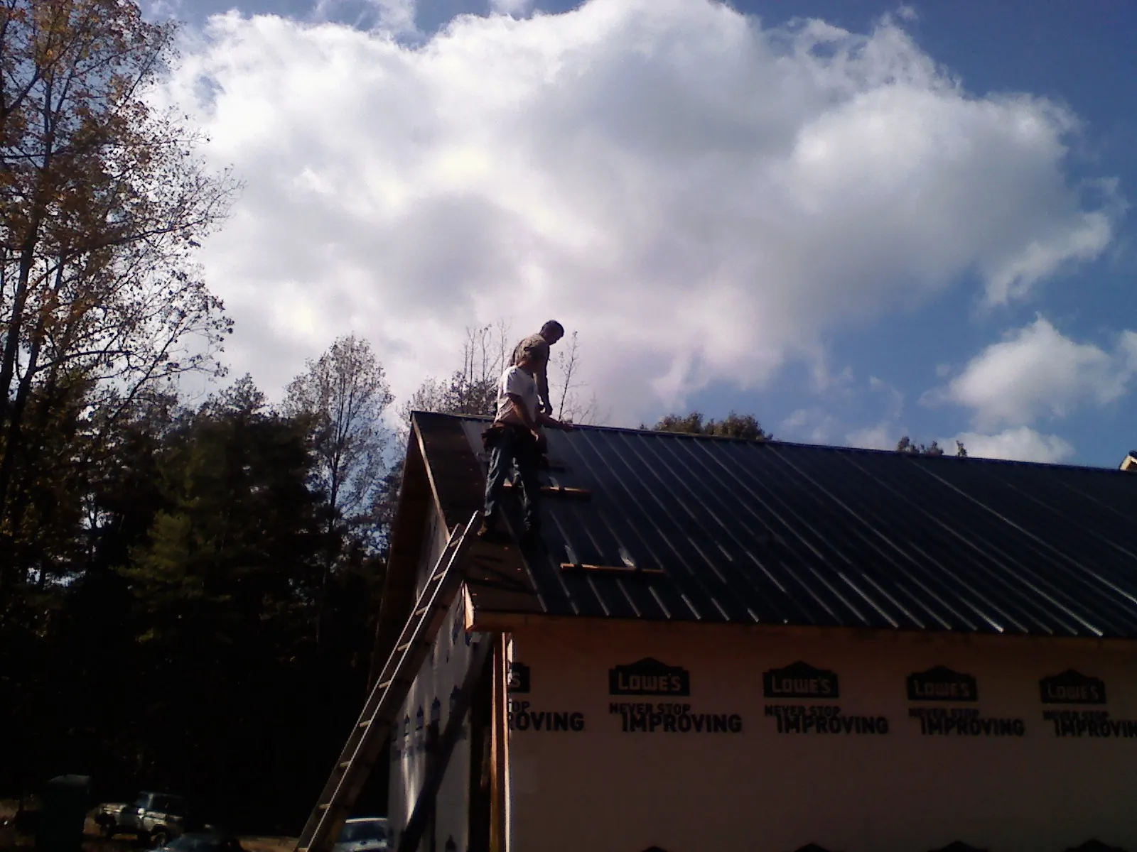 Roofer fastening dark metal panels high against a cloudy sky, from a Roof Inspection job in Purchase