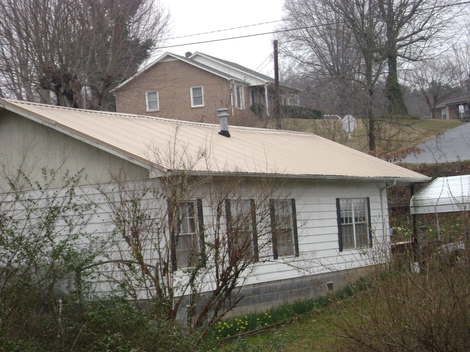 Tan metal roof on a white sided house set into a hillside — Commercial Roofing by Roofing Brothers in Purchase