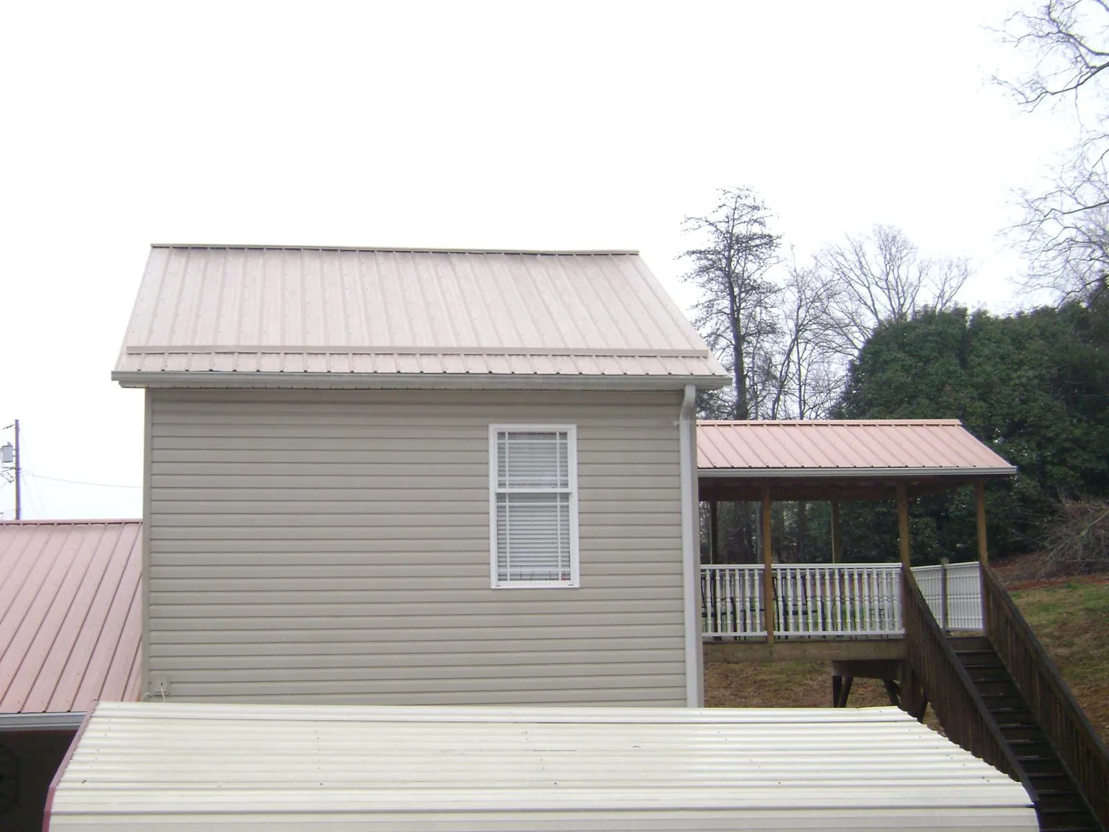Tan metal roofs on a two story addition and attached porch, from a Roof Replacement job in Purchase